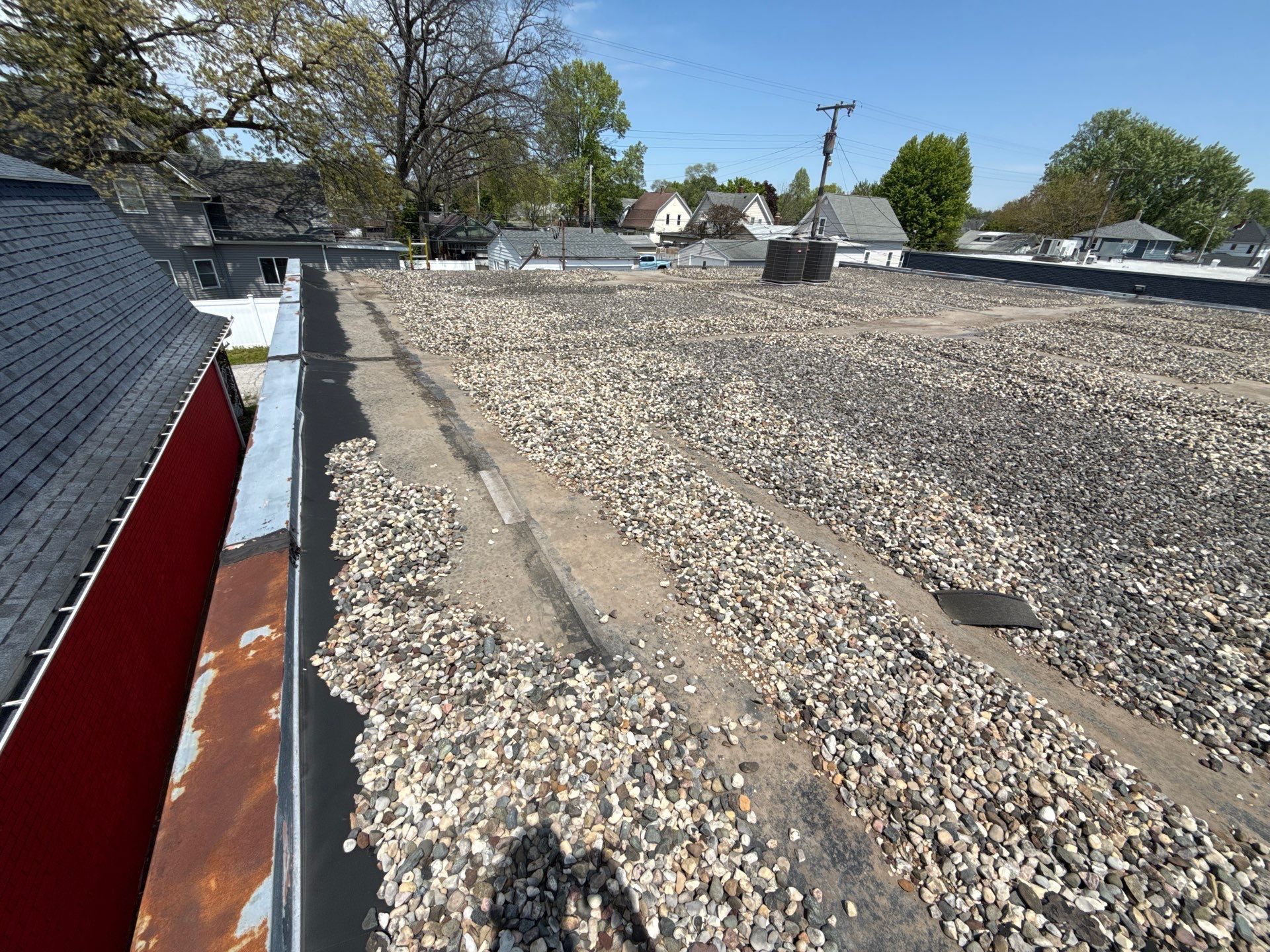 Gravel-covered flat rooftop with vents, skylights, and trees visible in the distance.