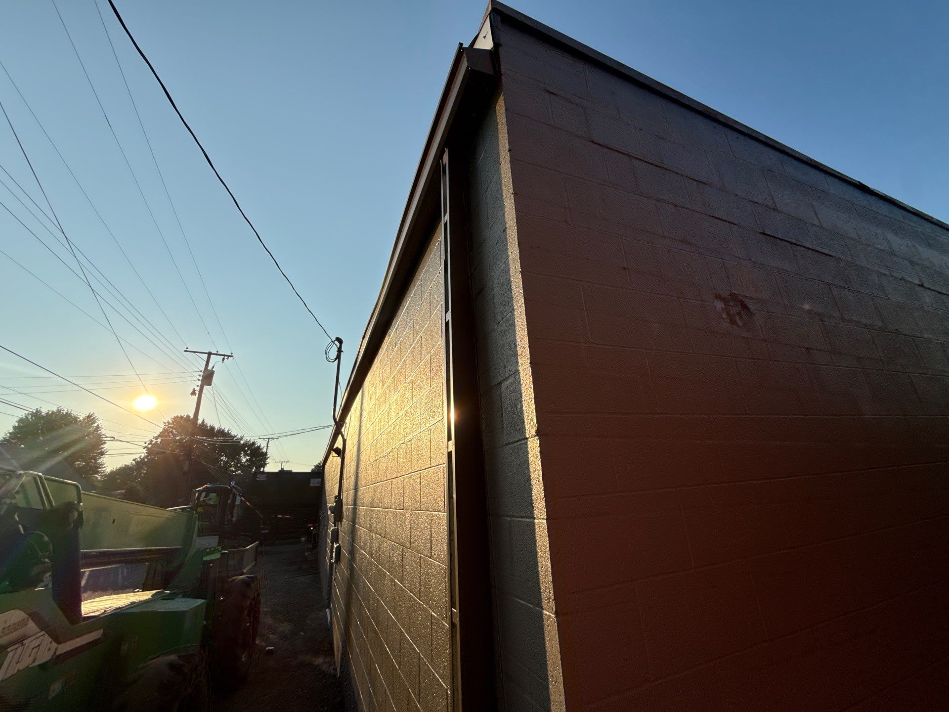 Sunlit backyard beside a house wall at sunset, with utility poles and power lines overhead
