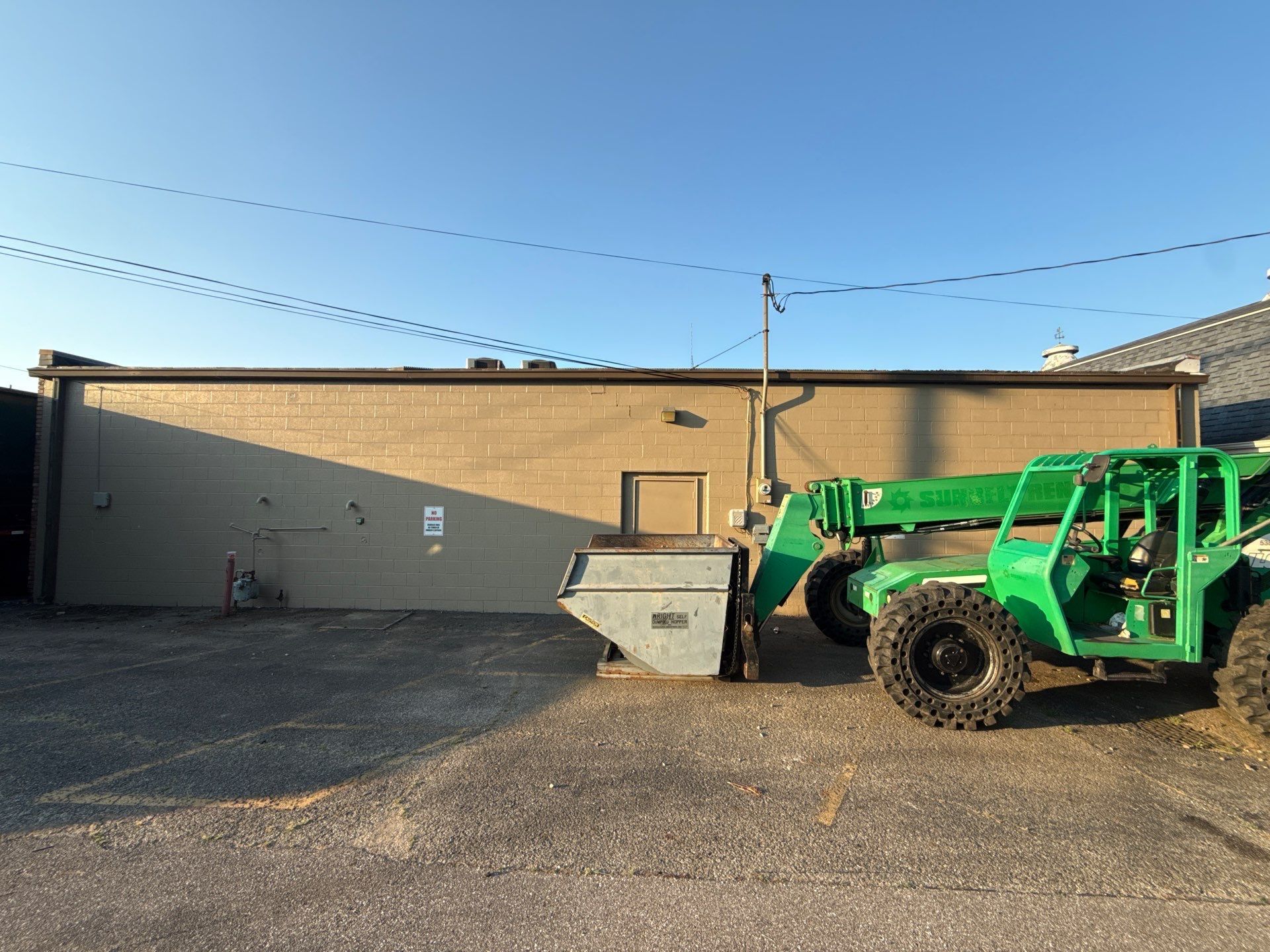 Green tractor with bucket parked beside a tan warehouse in a gravel lot under string lights