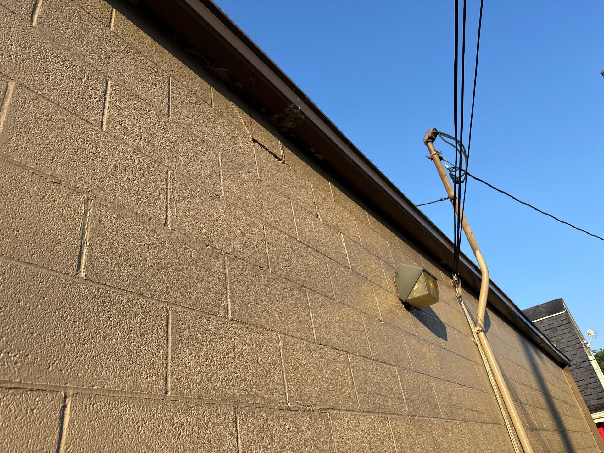Weathered beige wall with a slanted roof edge, utility pole, and power lines against a clear blue sky