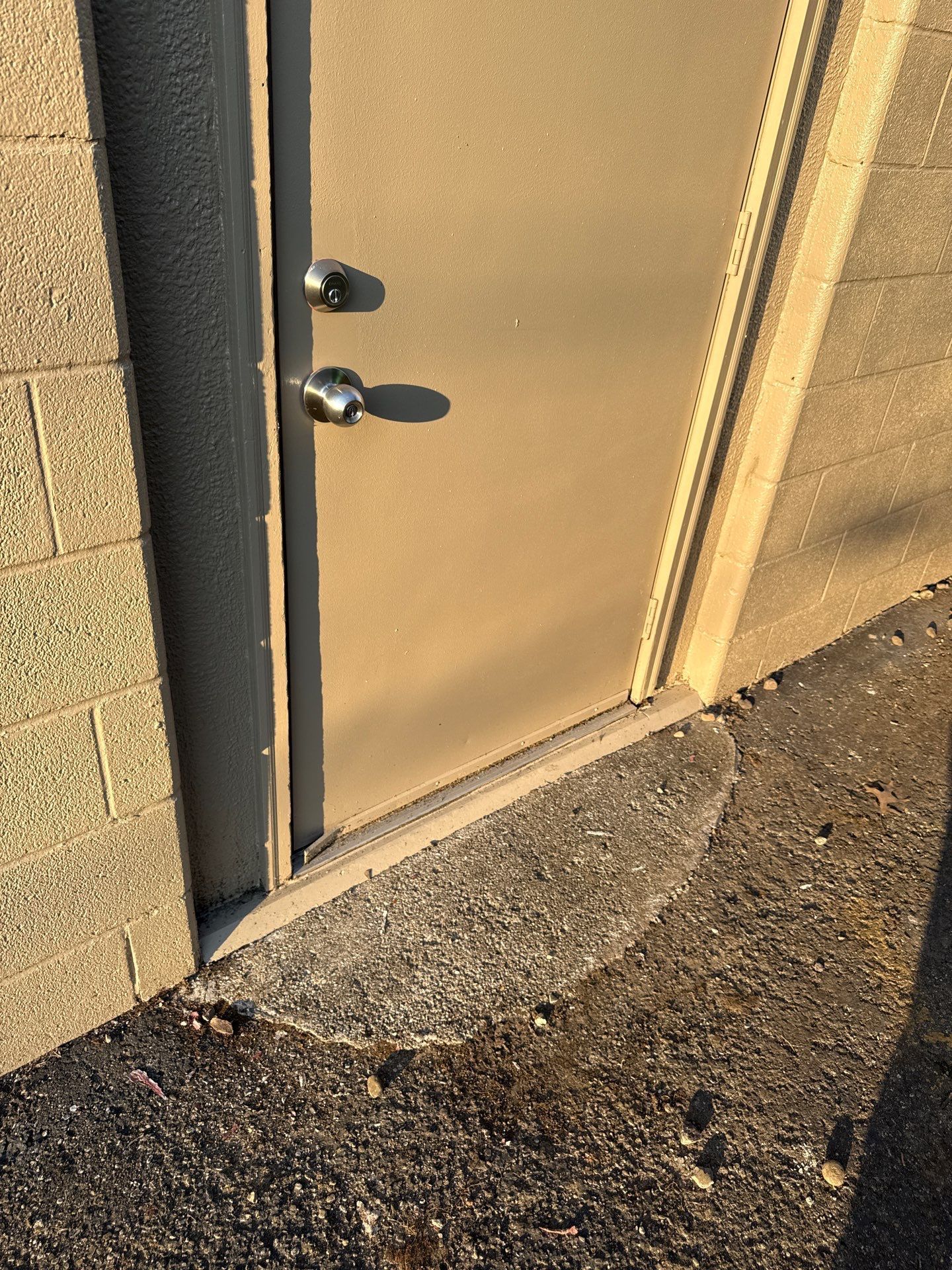 Close-up of a beige door with two dark knobs beside a textured wall and gravel ground.