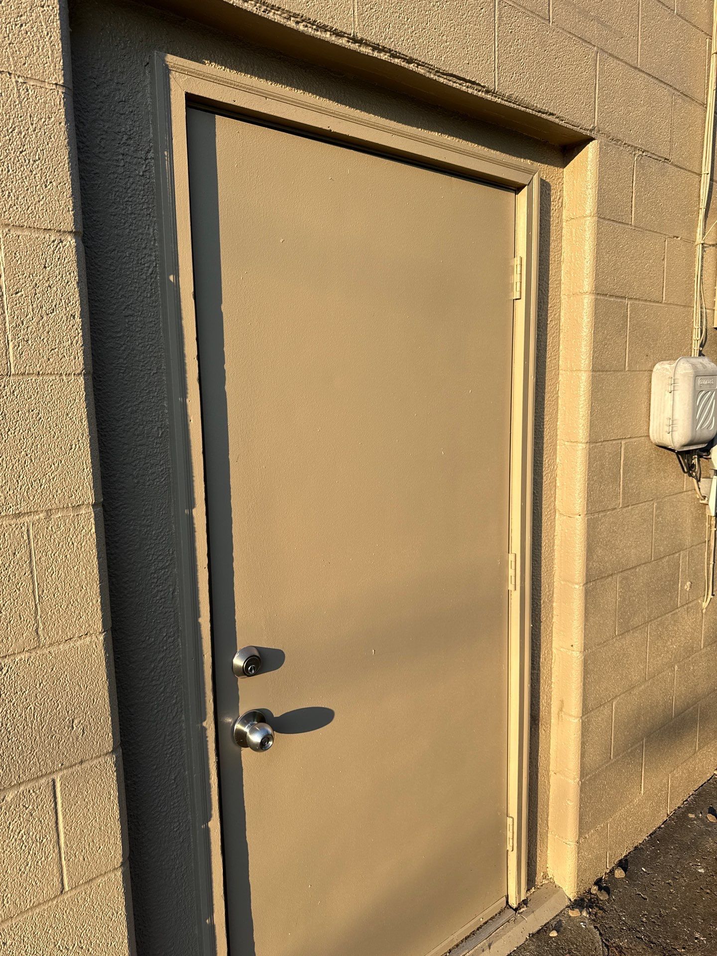Closed beige metal door in a stucco wall, lit by warm sunlight.