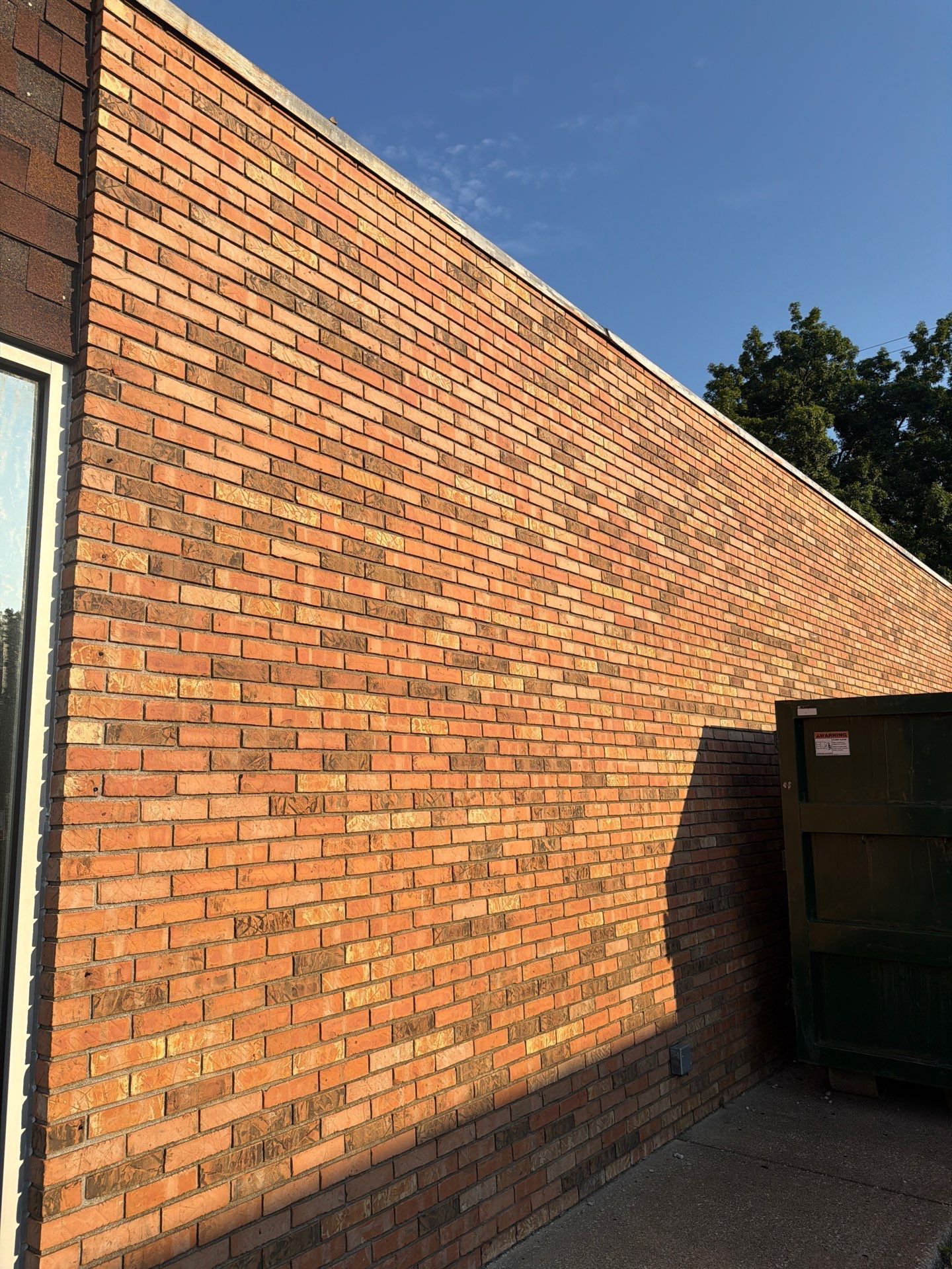 Brick wall in sunlight beside a dark green container under a clear blue sky