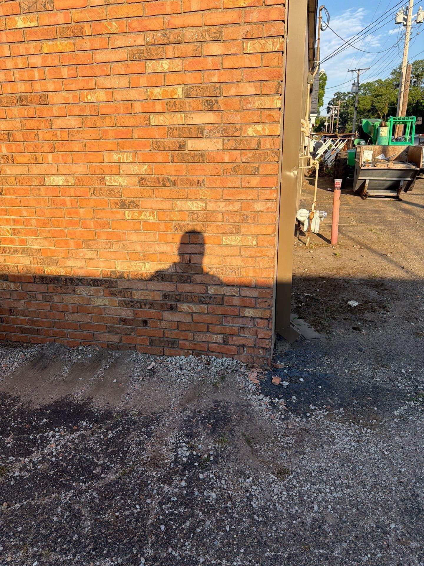 Brick wall beside a gravel lot with construction equipment in the background and a person’s shadow in front