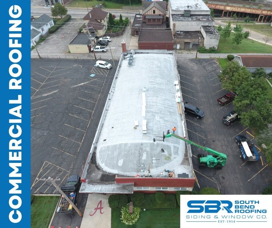 Aerial view of commercial roofing crew repairing a flat roof with a green boom lift.