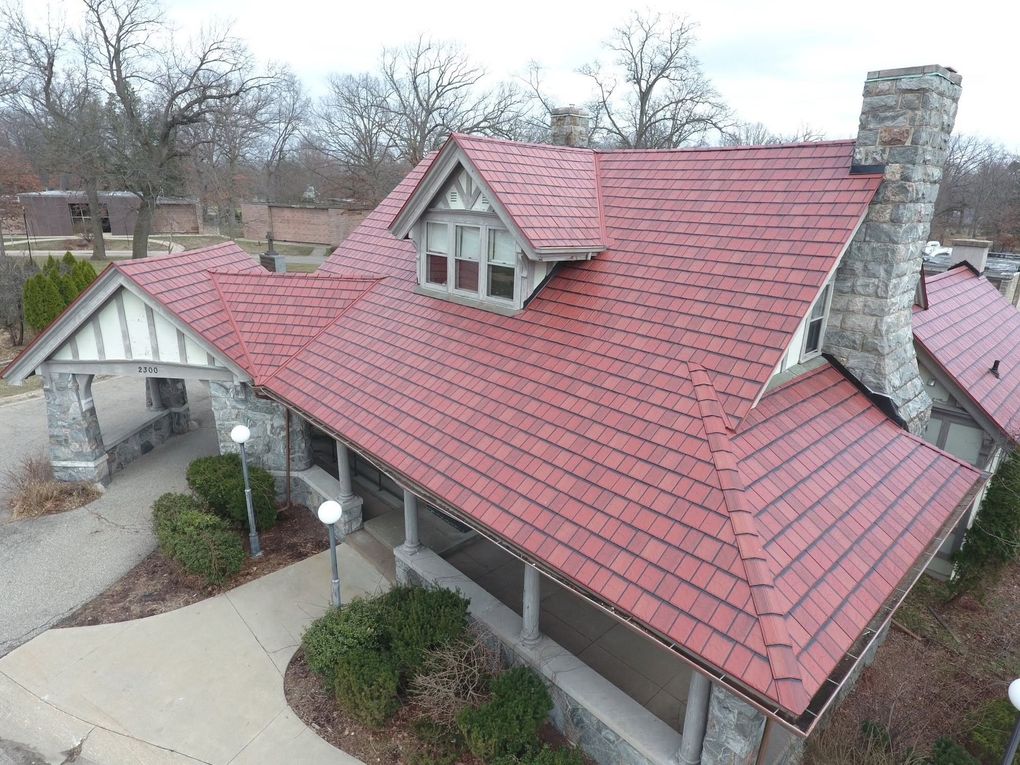 Aerial view of a house with a red shingled roof, stone chimney, and covered front porch.