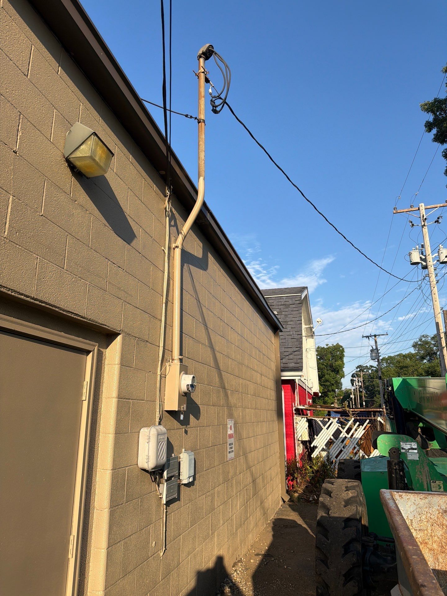 Narrow alley beside a tan building with utility poles, wires, and blue sky overhead