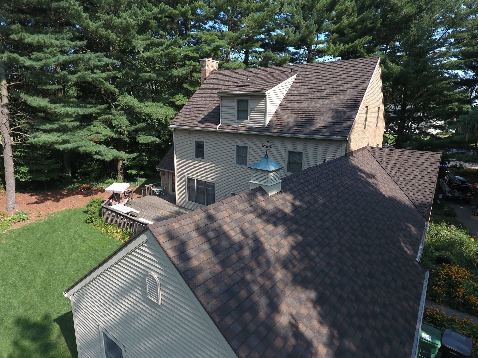 Aerial view of a gray house with a sloped roof, surrounded by trees and a green yard.