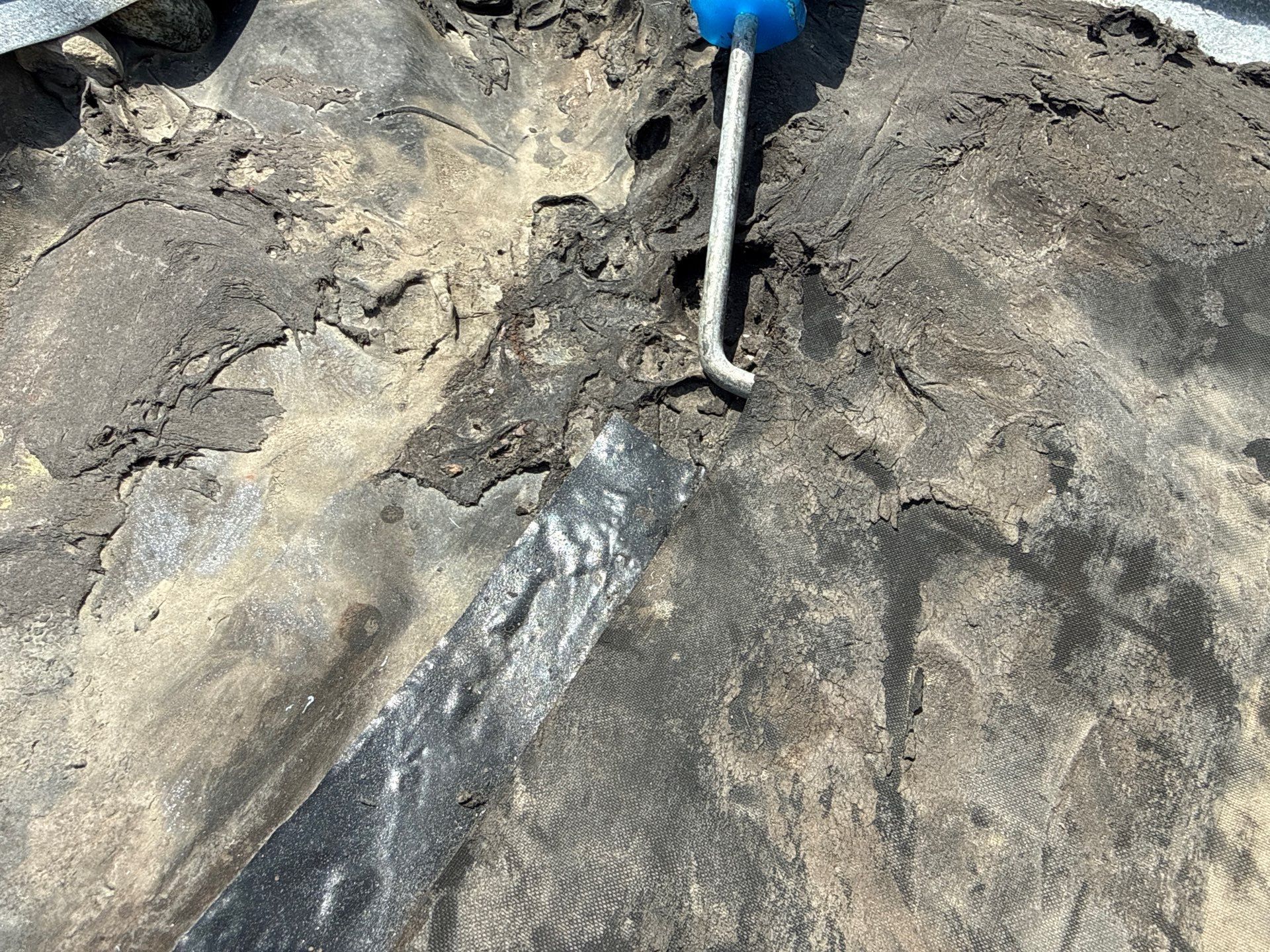 Close-up of a shovel scraping wet mud beside a dark trench in rocky ground