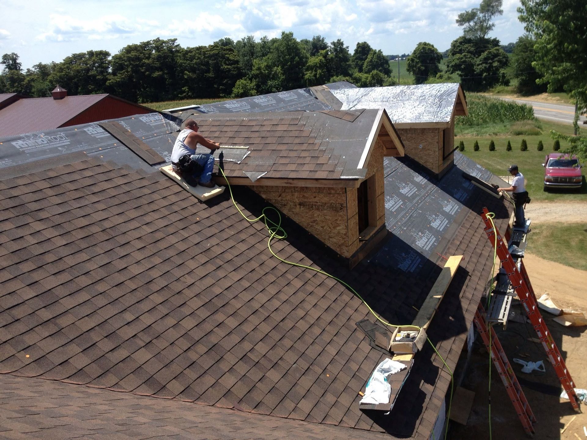 Workers repairing brown shingle roof on a house, with ladders and tools visible