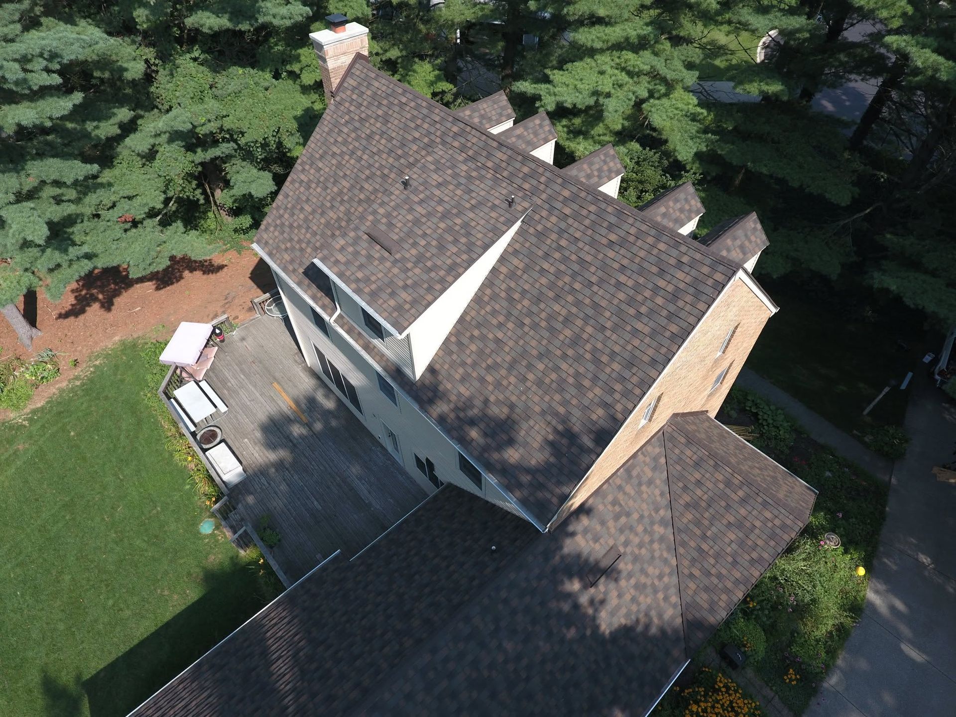 Aerial view of a house with a dark roof, driveway, and surrounding trees