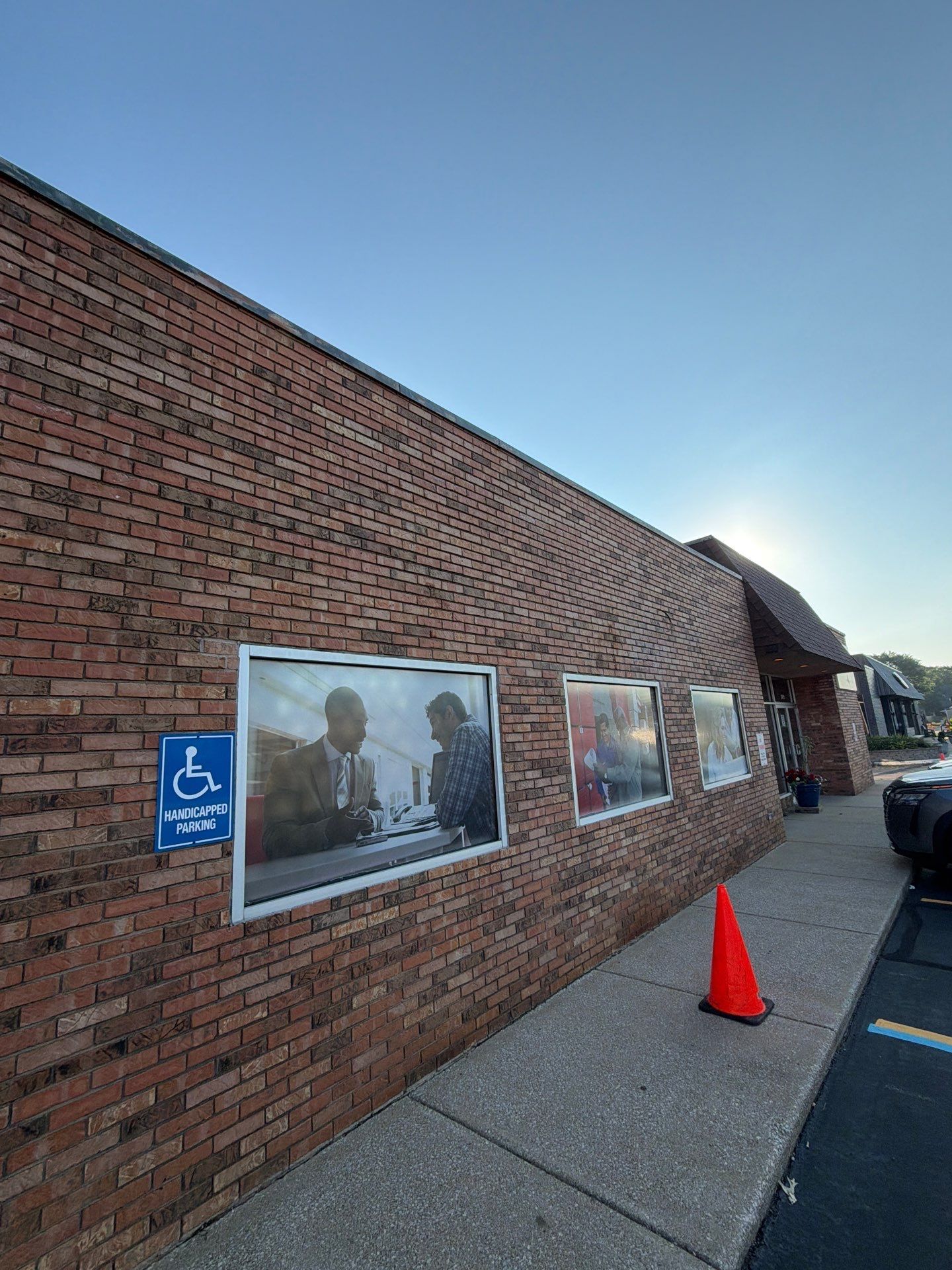 Brick wall with framed posters, a blue accessibility sign, and an orange cone beside a sidewalk.
