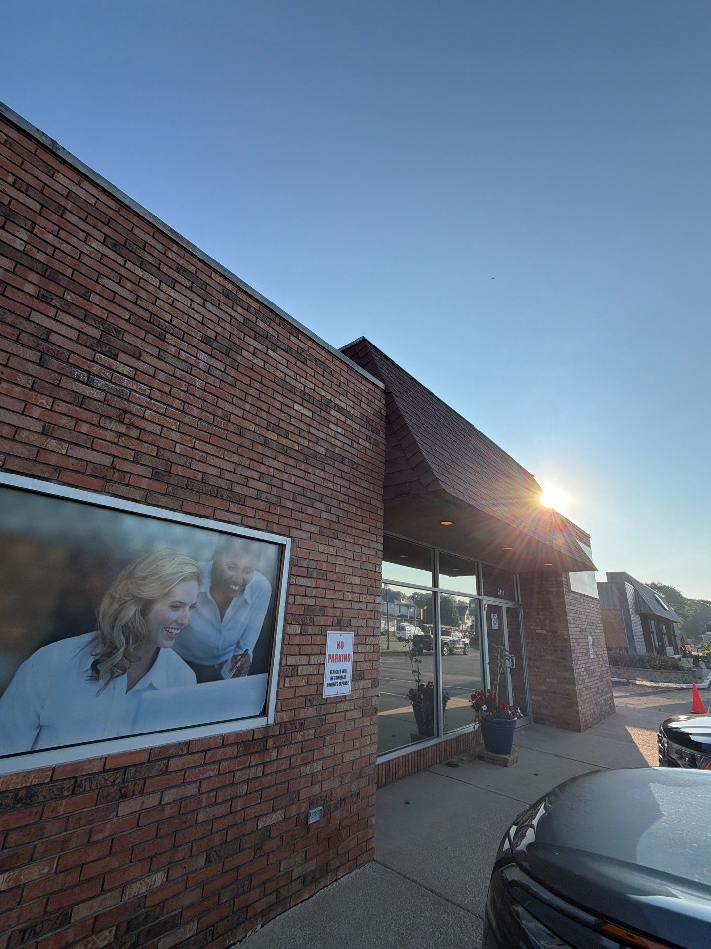 Brick storefront with a large window poster, sun glare, and parked car in front