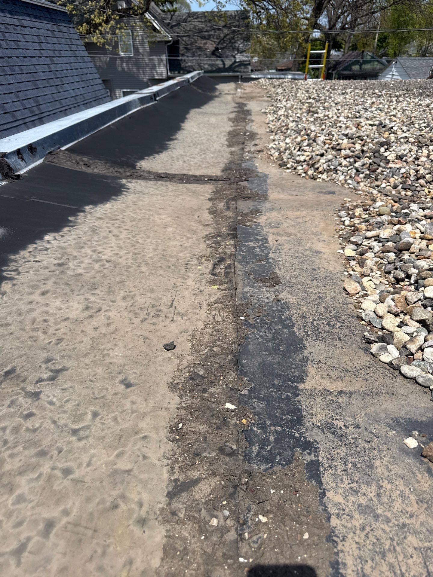 Cracked concrete path beside a building, with a gravel bed and striped caution barrier in sunlight