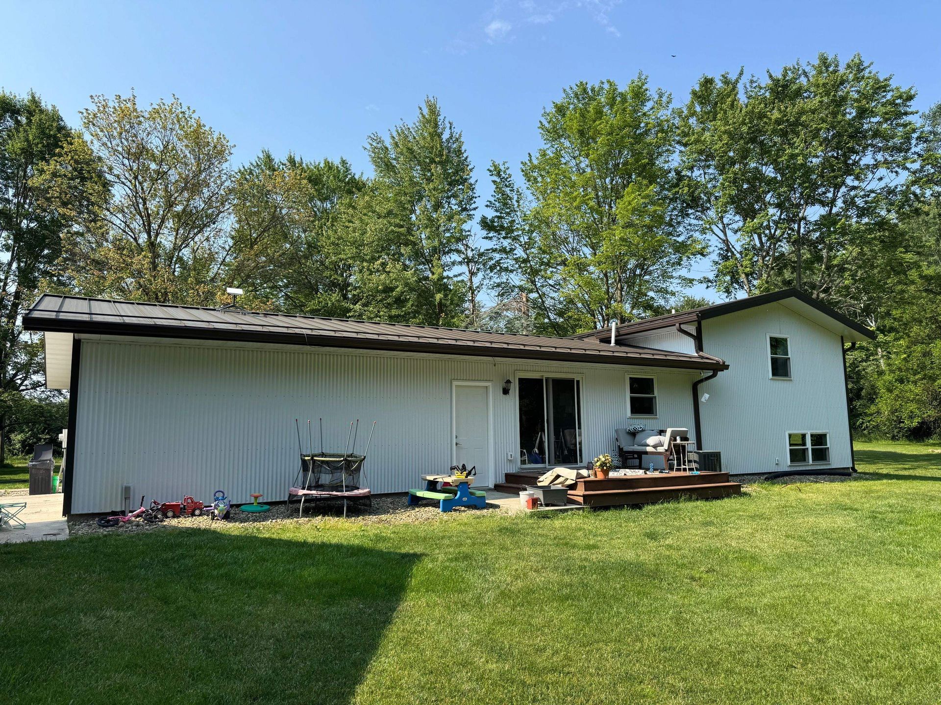 Backyard with a white house, wooden deck, and grassy lawn under trees
