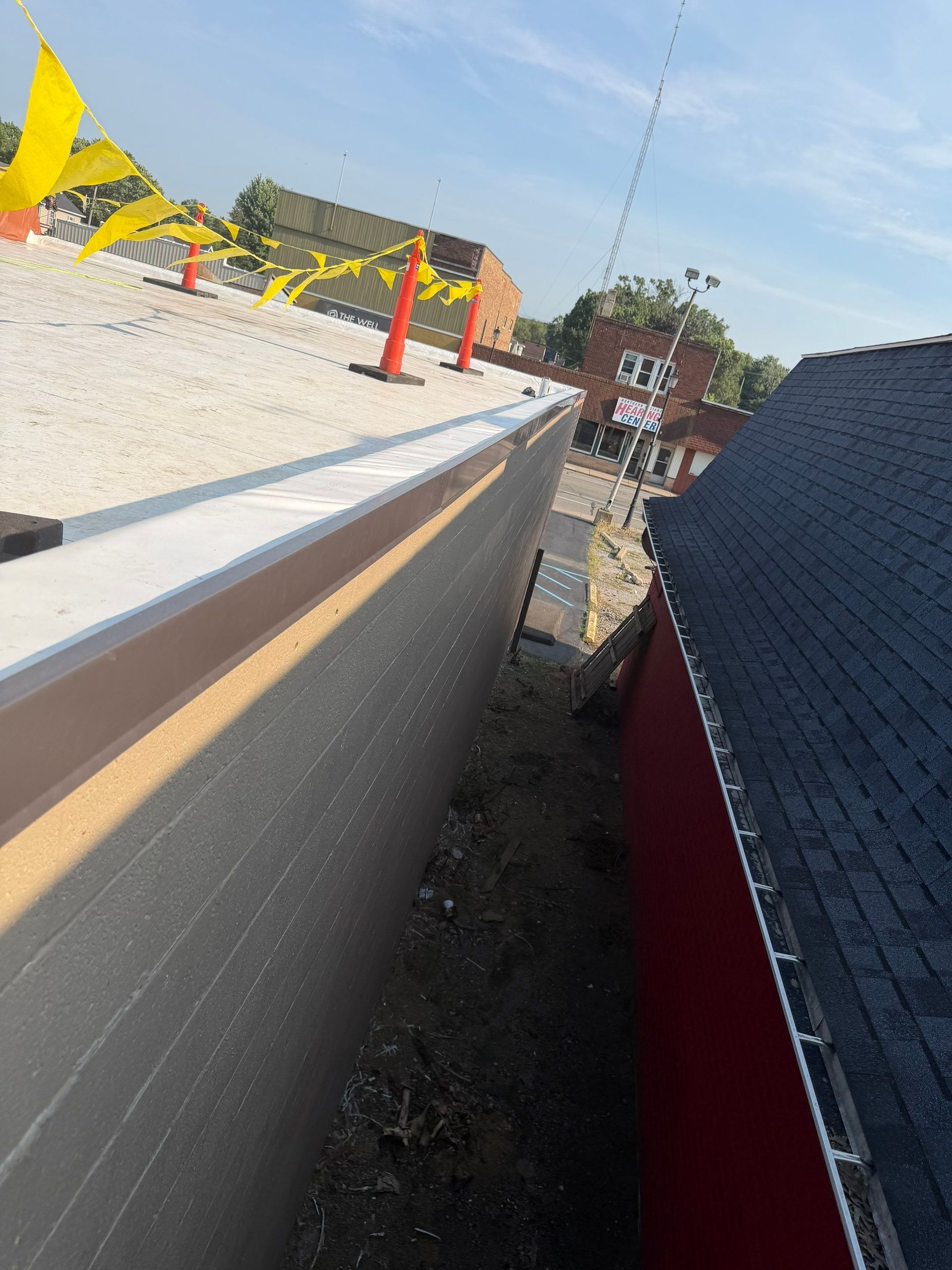 Roof edge and rooftop construction site with orange cones, gravel, and nearby buildings under a blue sky
