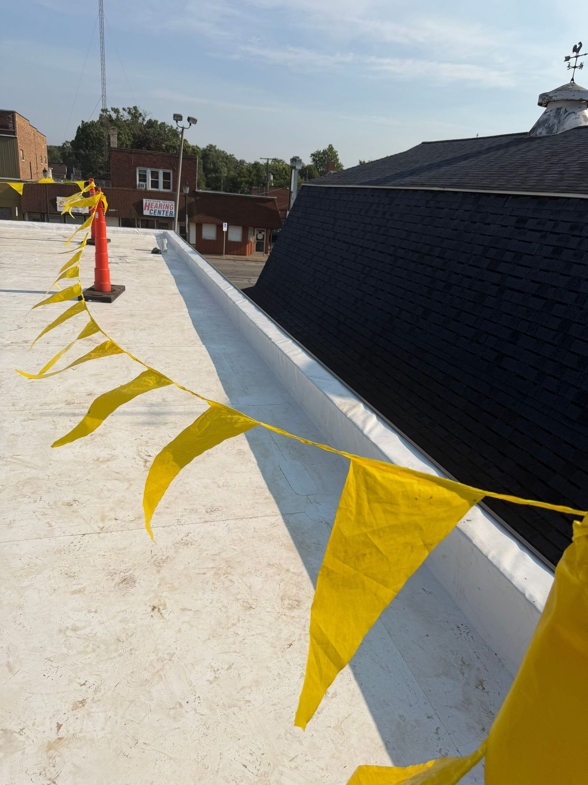 Rooftop under construction with yellow caution tape and a large black vent pipe.