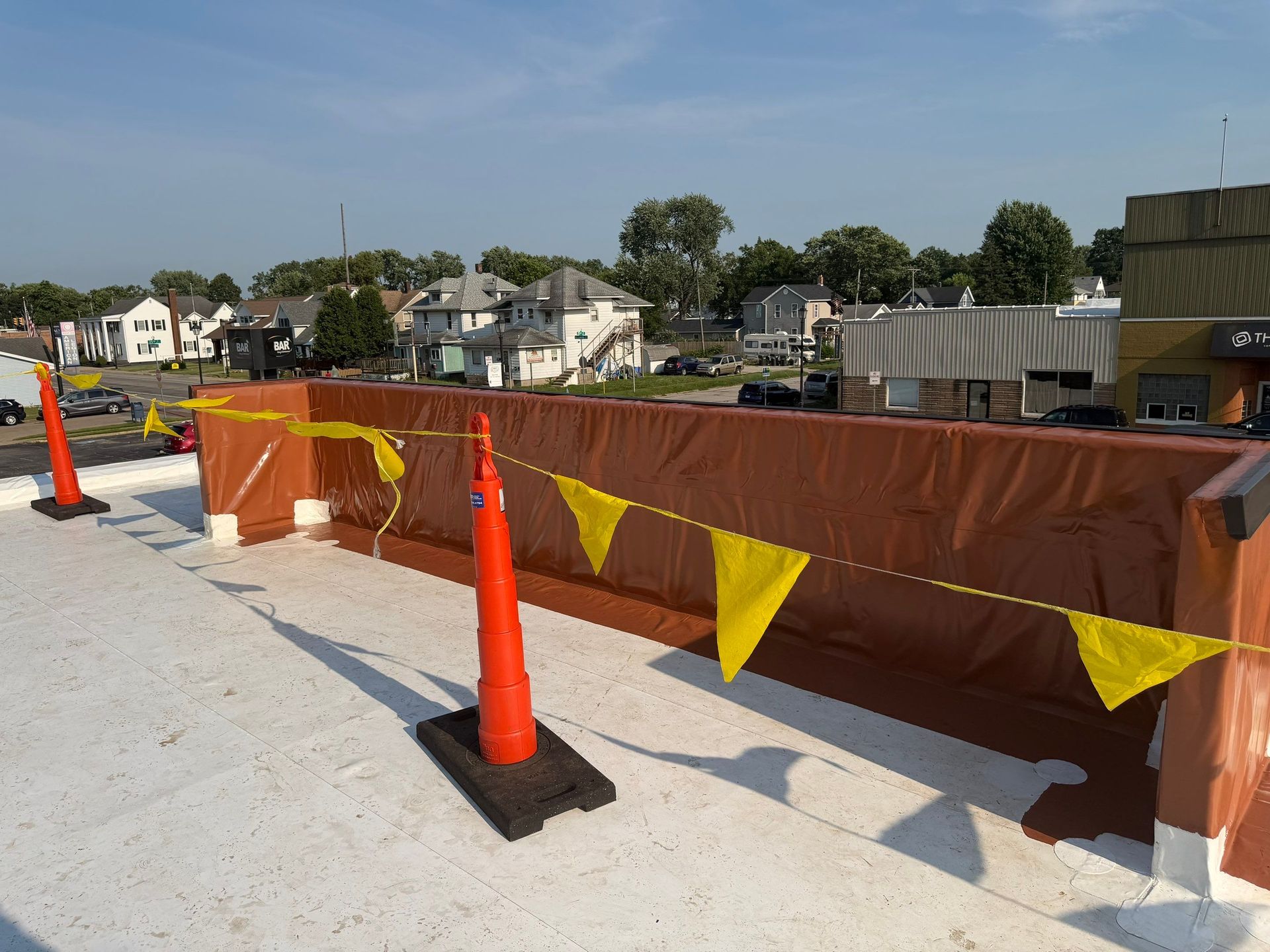 Orange safety fencing and cones around a construction area beside a waterfront, with houses in the background