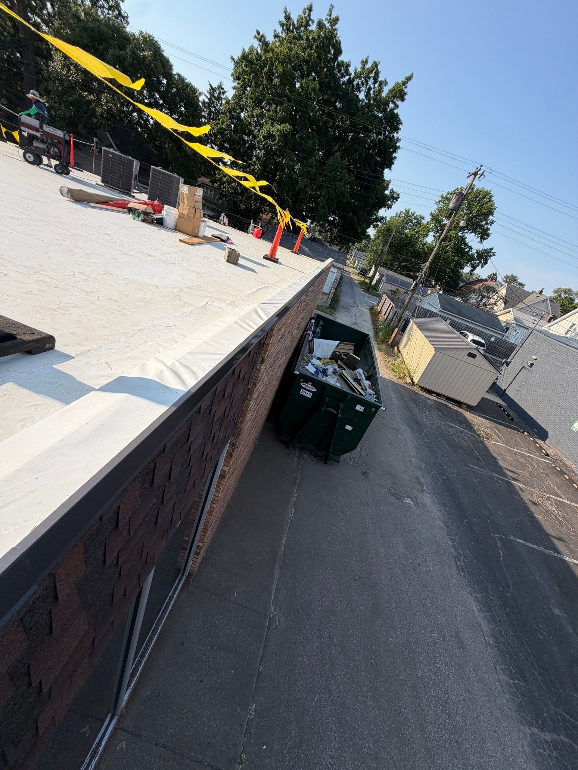 Tilted sidewalk beside a brick wall with green trash bins and yellow caution tape under a sunny sky