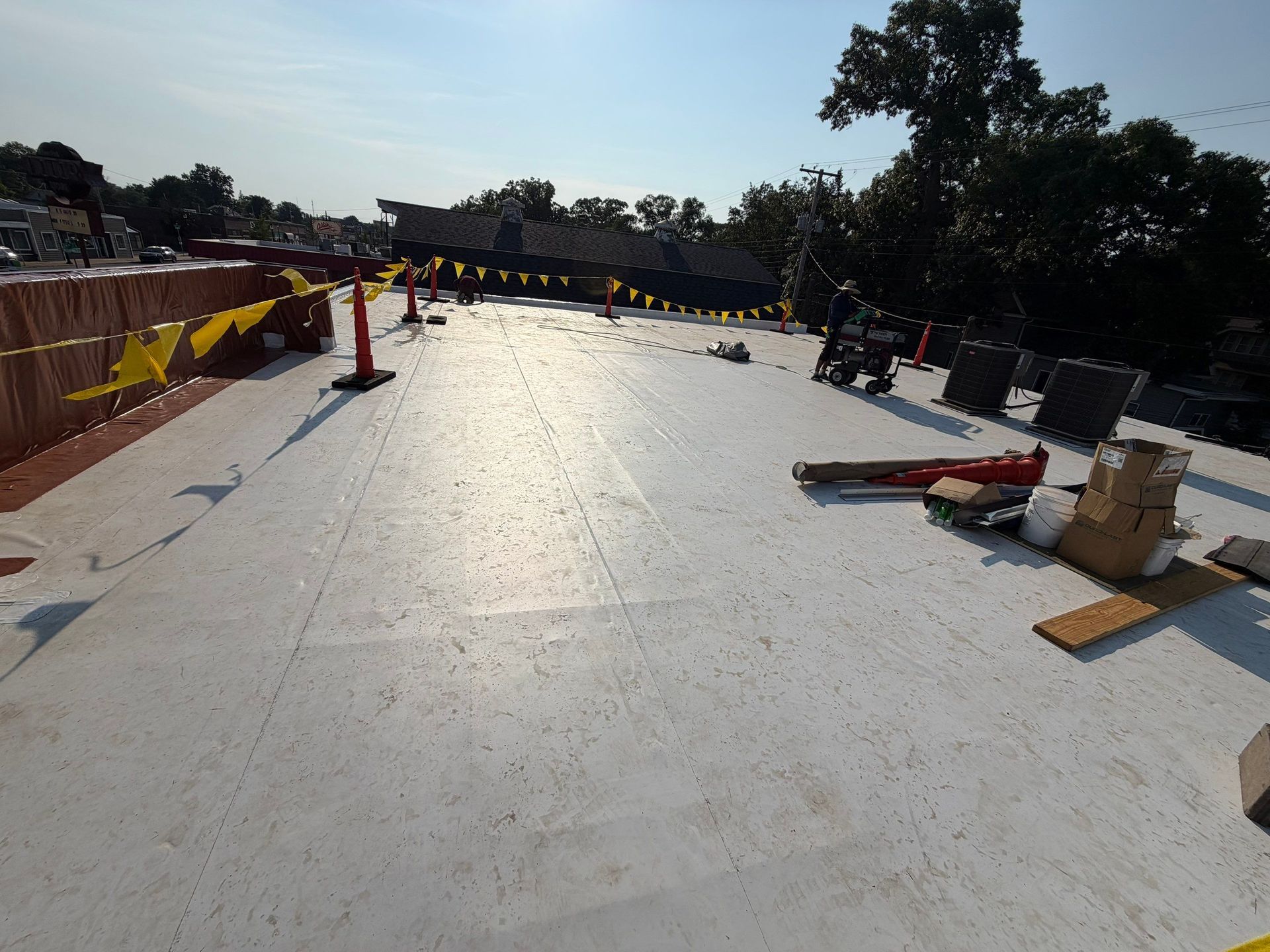 Rooftop construction site with workers, safety cones, and materials in bright sunlight