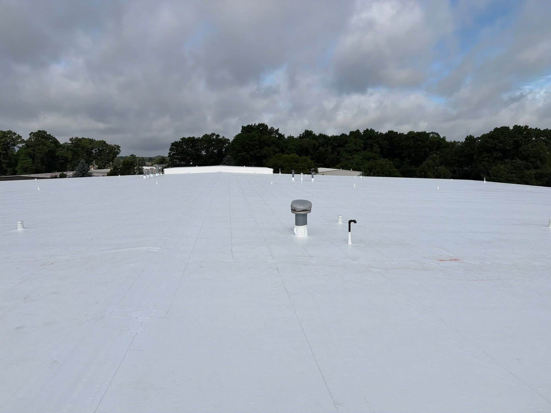 Flat white rooftop with vents under a cloudy sky, trees in the distance