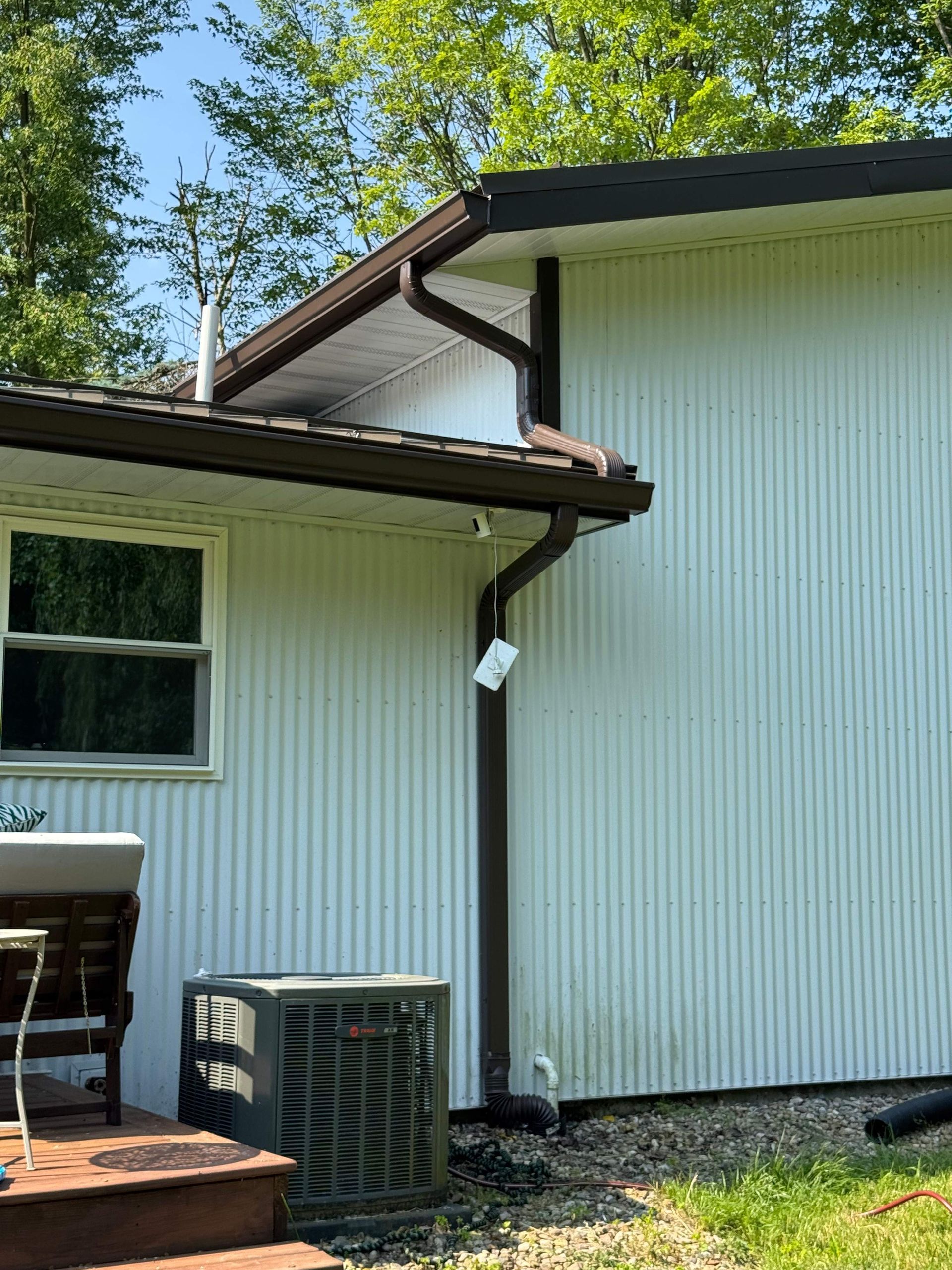 White-sided house exterior with roof, gutter, deck, and air conditioner unit under trees