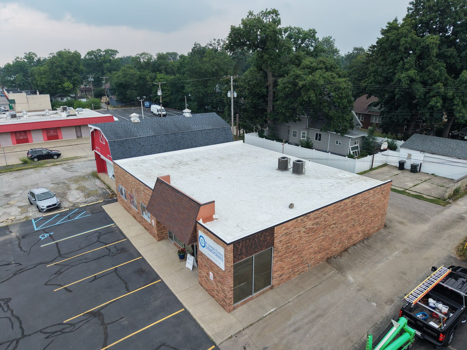 Aerial view of a brick commercial building with a white roof, parking lot, and nearby trees.