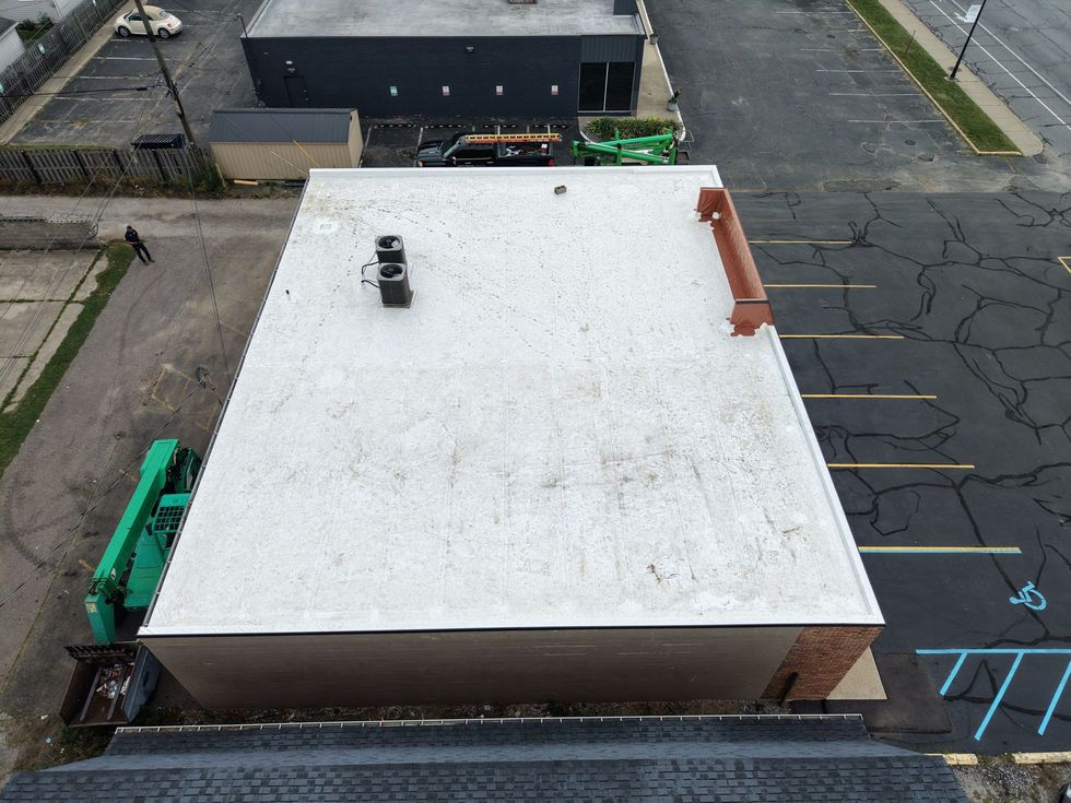 Overhead view of a flat-roofed white building in an empty parking lot, with dumpsters and a few parked vehicles nearby