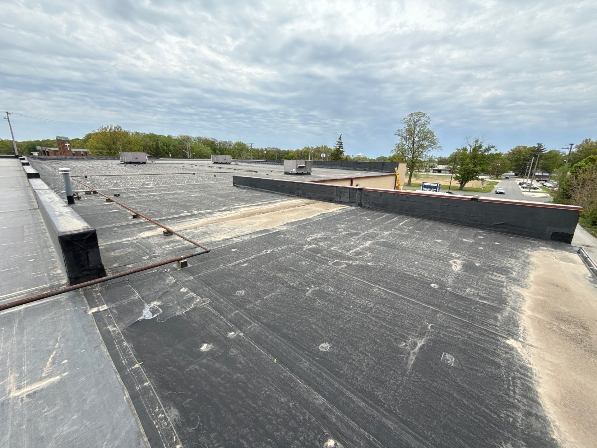 Flat commercial rooftop with gravel, black membrane, vents, and cloudy sky above.