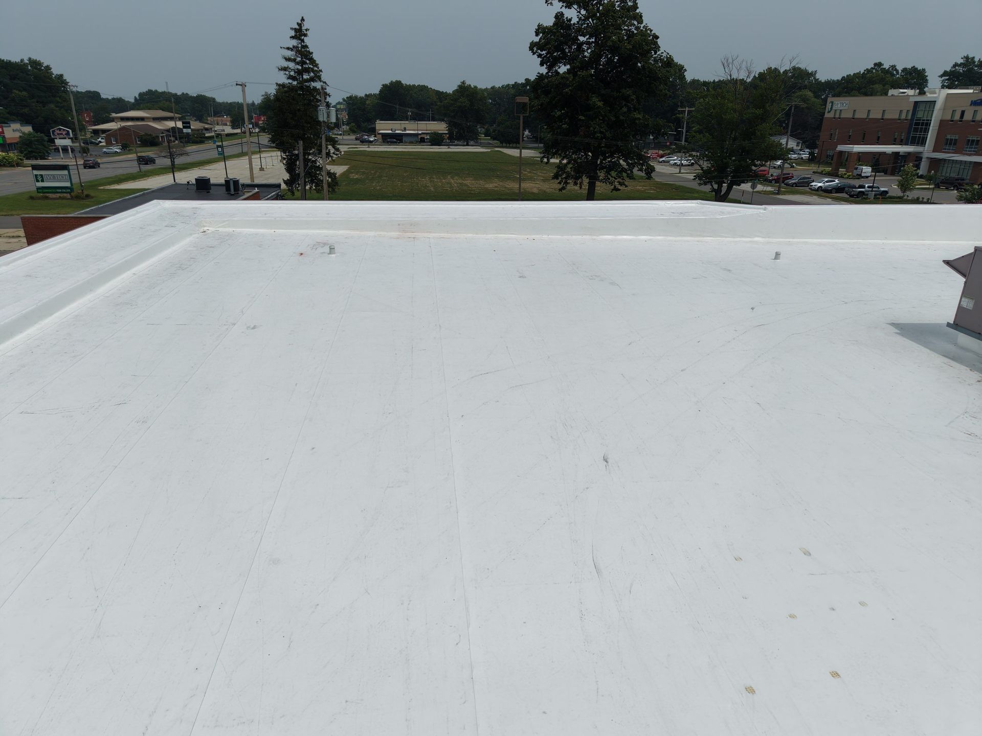 Flat white rooftop overlooking a suburban neighborhood and trees under a clear sky