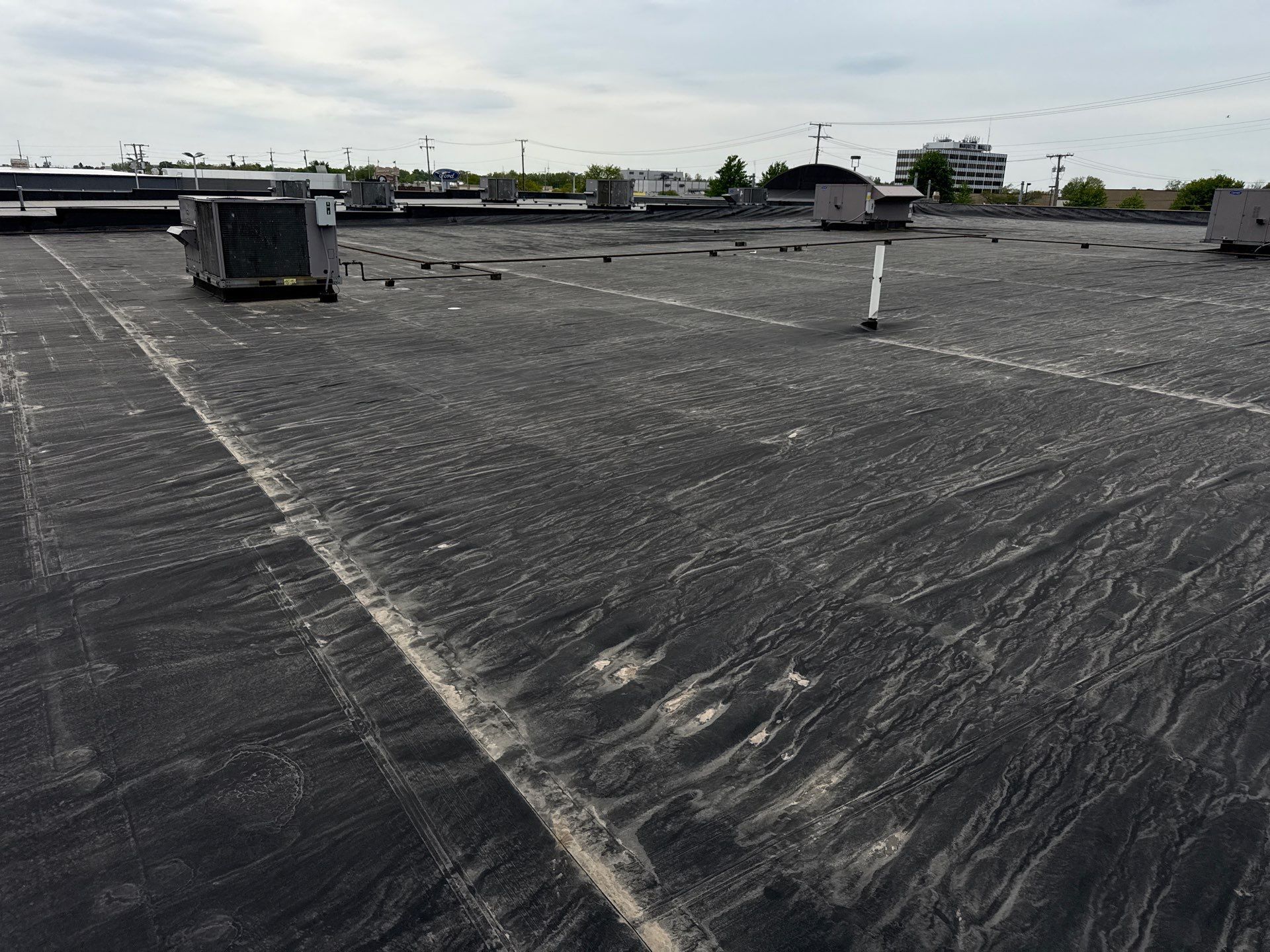 Flat rooftop with gravel surface, vents, and distant buildings under a cloudy sky