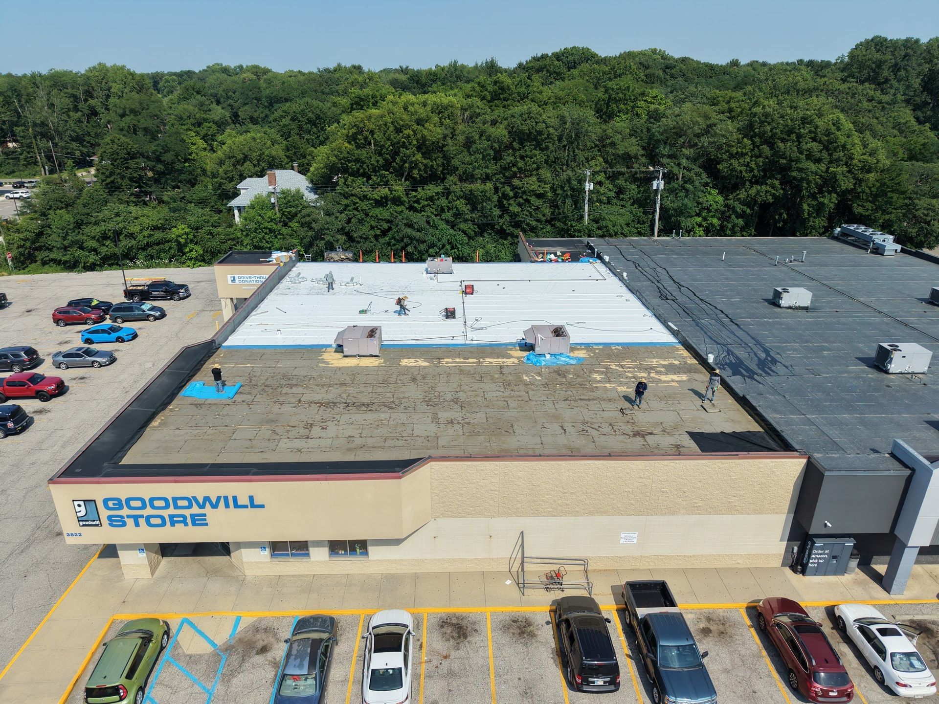 Aerial view of a Goodwill store with parking lot, cars, and trees behind it.