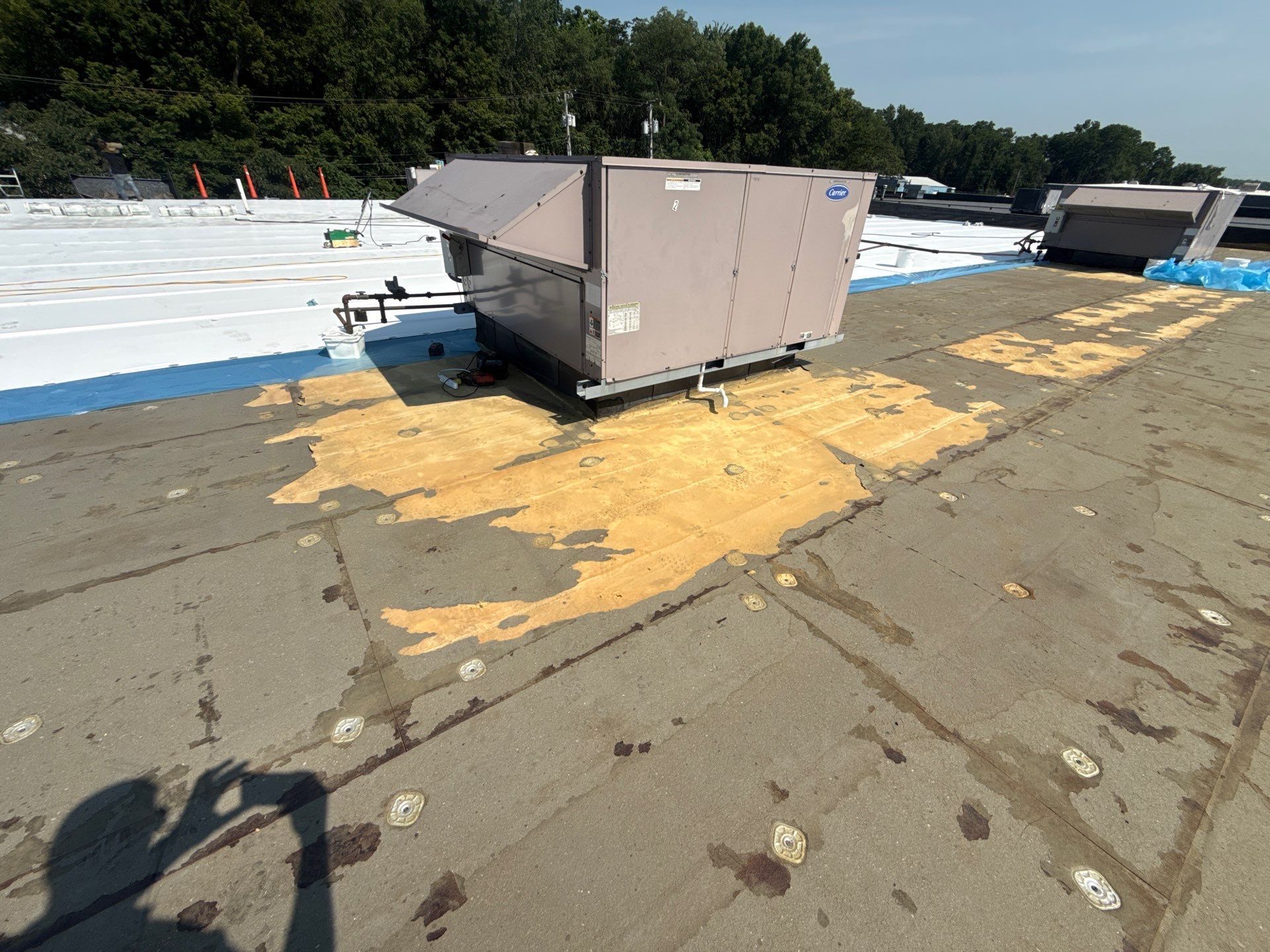 Beige rooftop HVAC unit on a flat roof with yellow spill stain and trees in the background