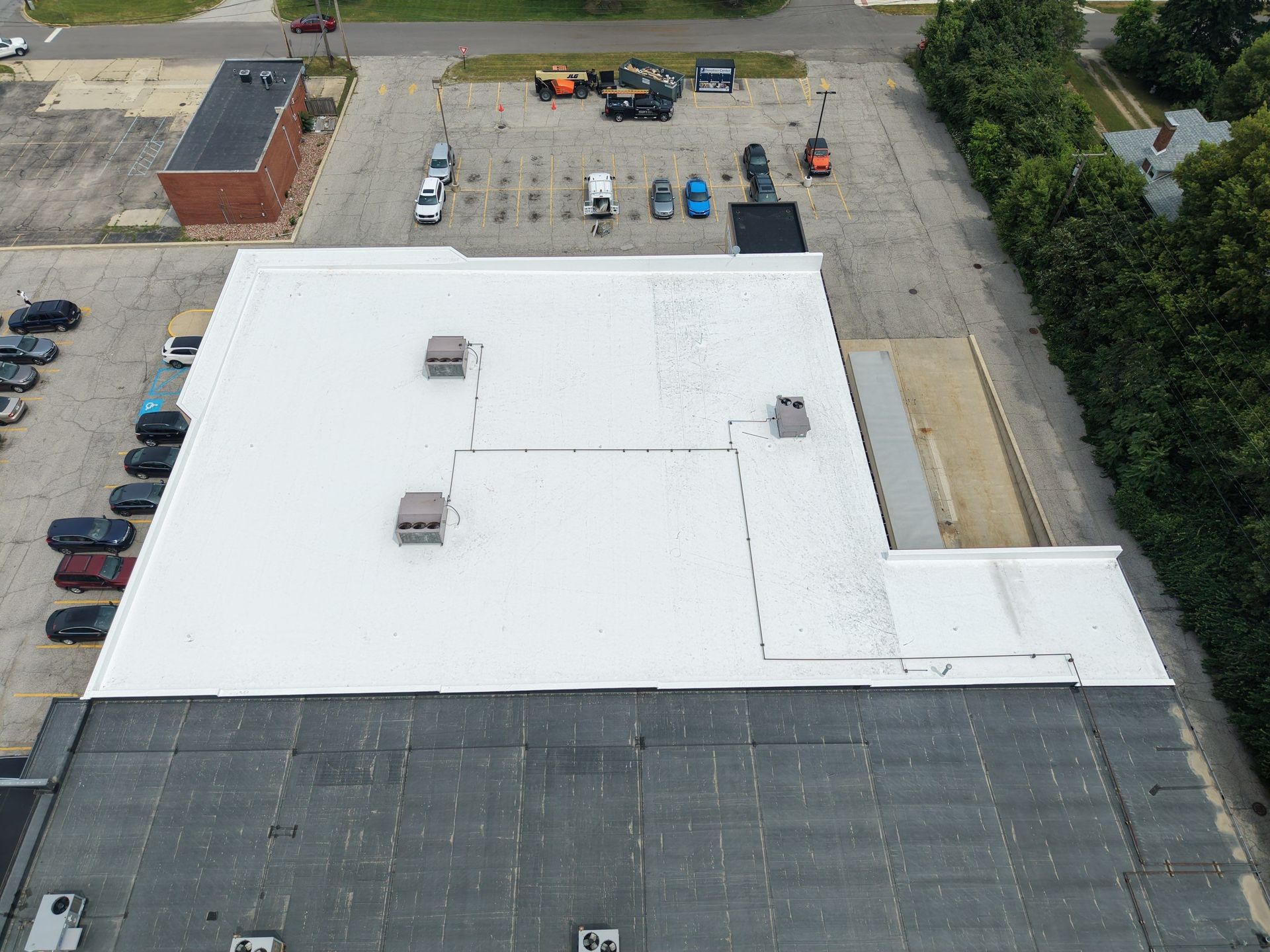 Aerial view of a large white-roofed building with parking lots and cars on both sides.