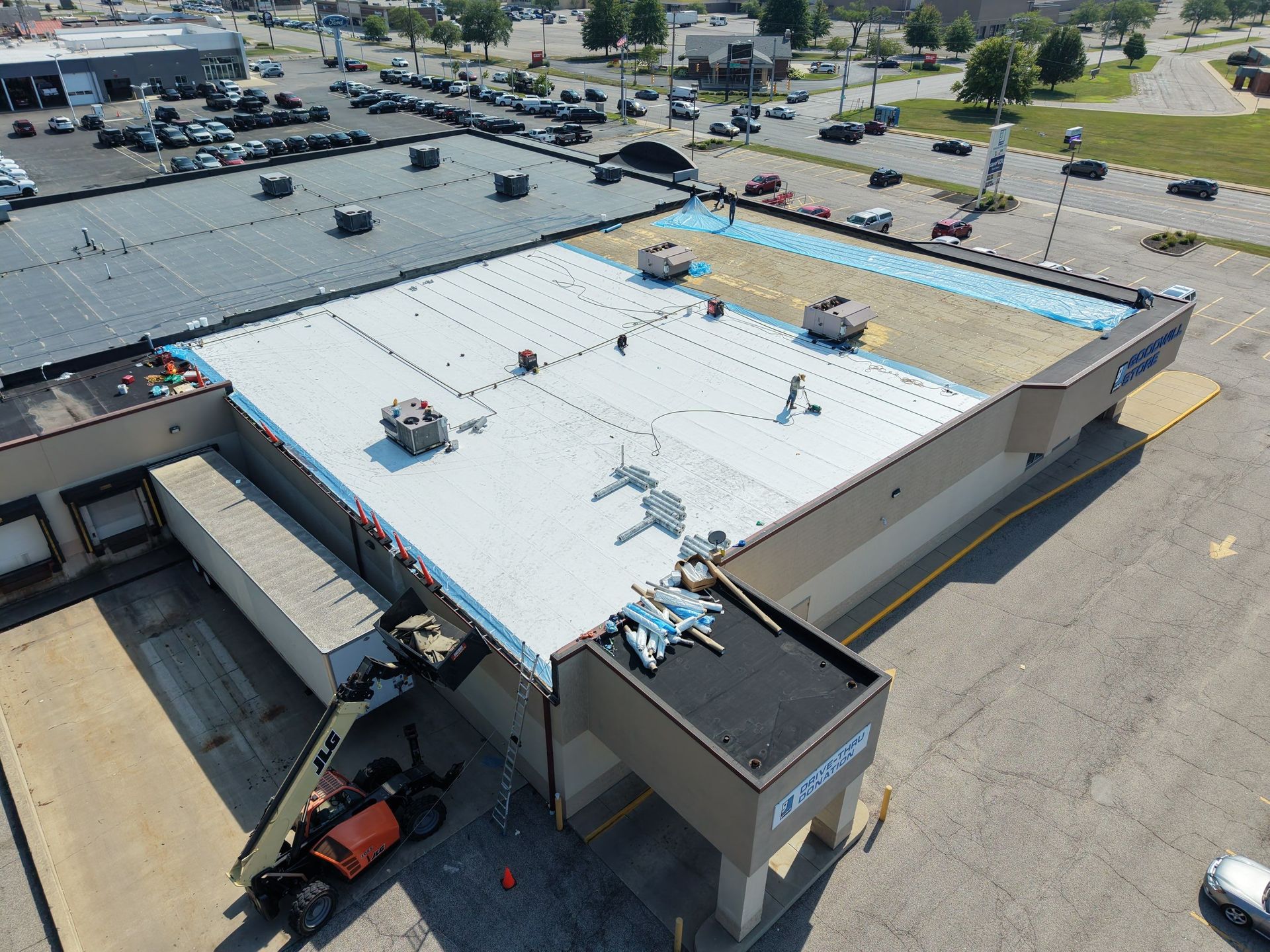 Aerial view of a large flat-roofed commercial building with parked cars and a street nearby.