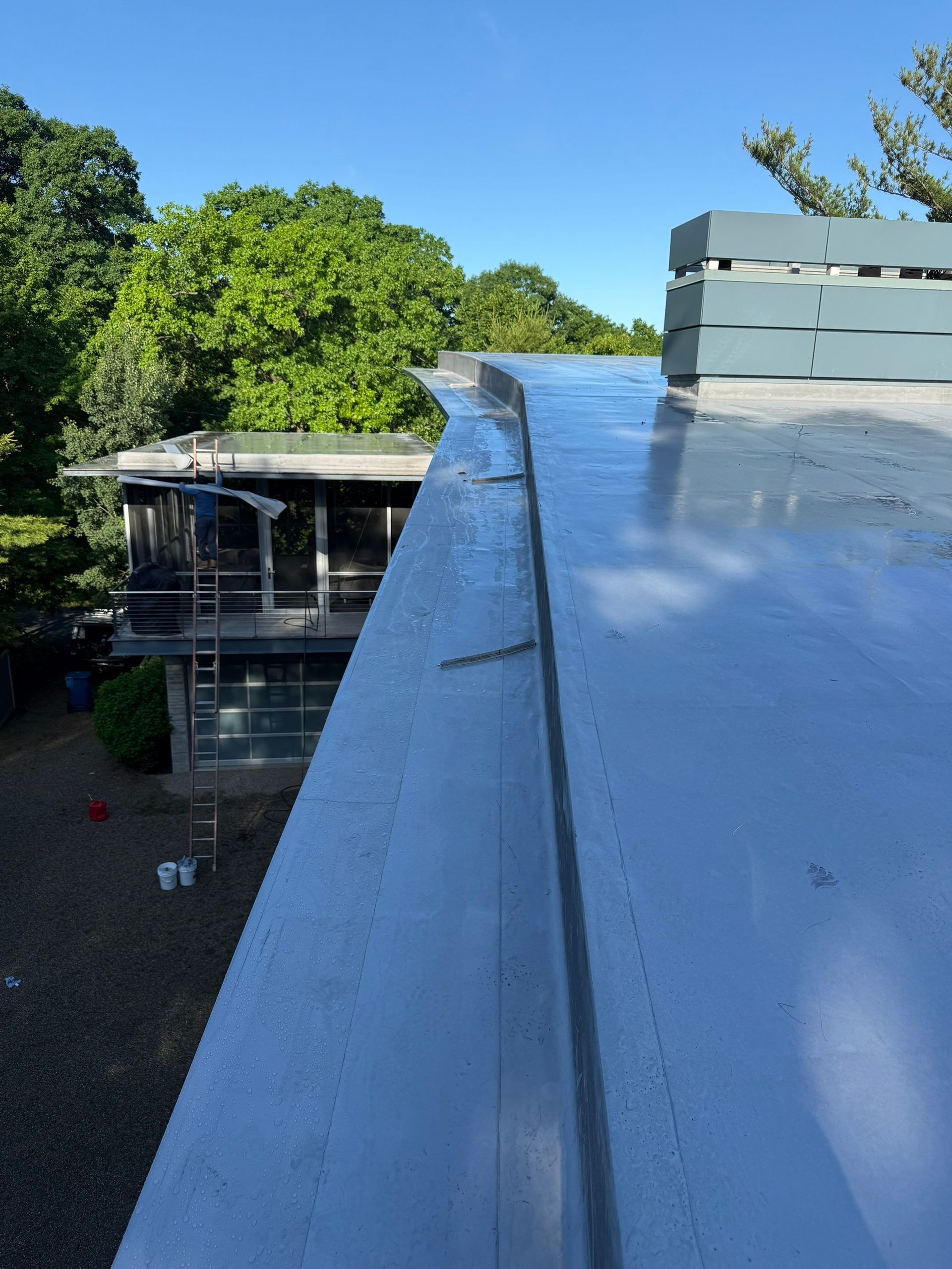 Flat rooftop with a reflective silver surface, vents, and trees in the background under a clear blue sky