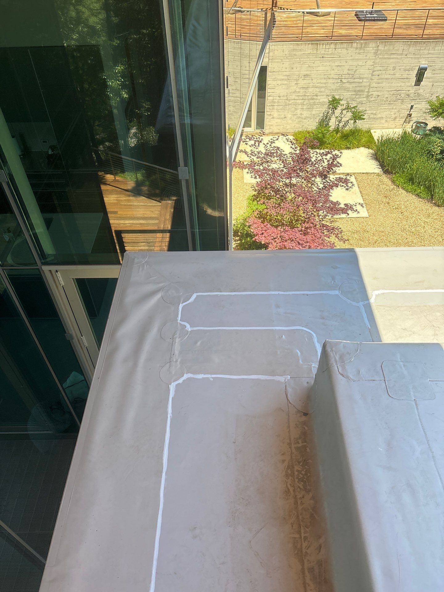Concrete balcony railing beside a glass wall, overlooking a garden and stone courtyard below