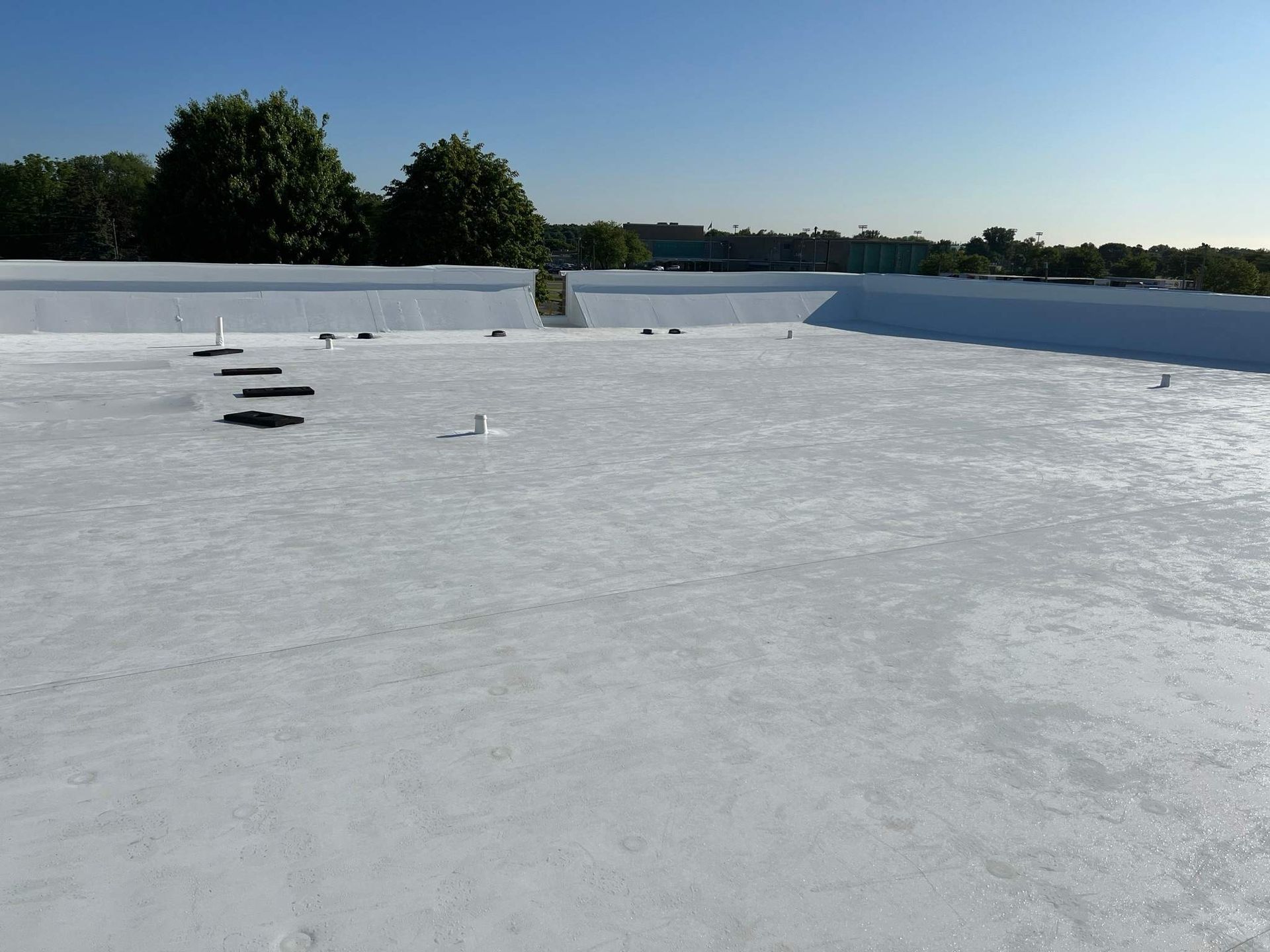 Snow-covered flat rooftop with a few vents and trees in the distance