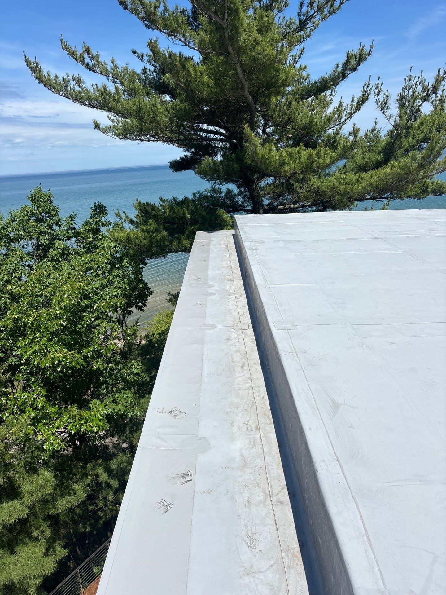 White rooftop edge overlooking blue ocean and green trees on a sunny day