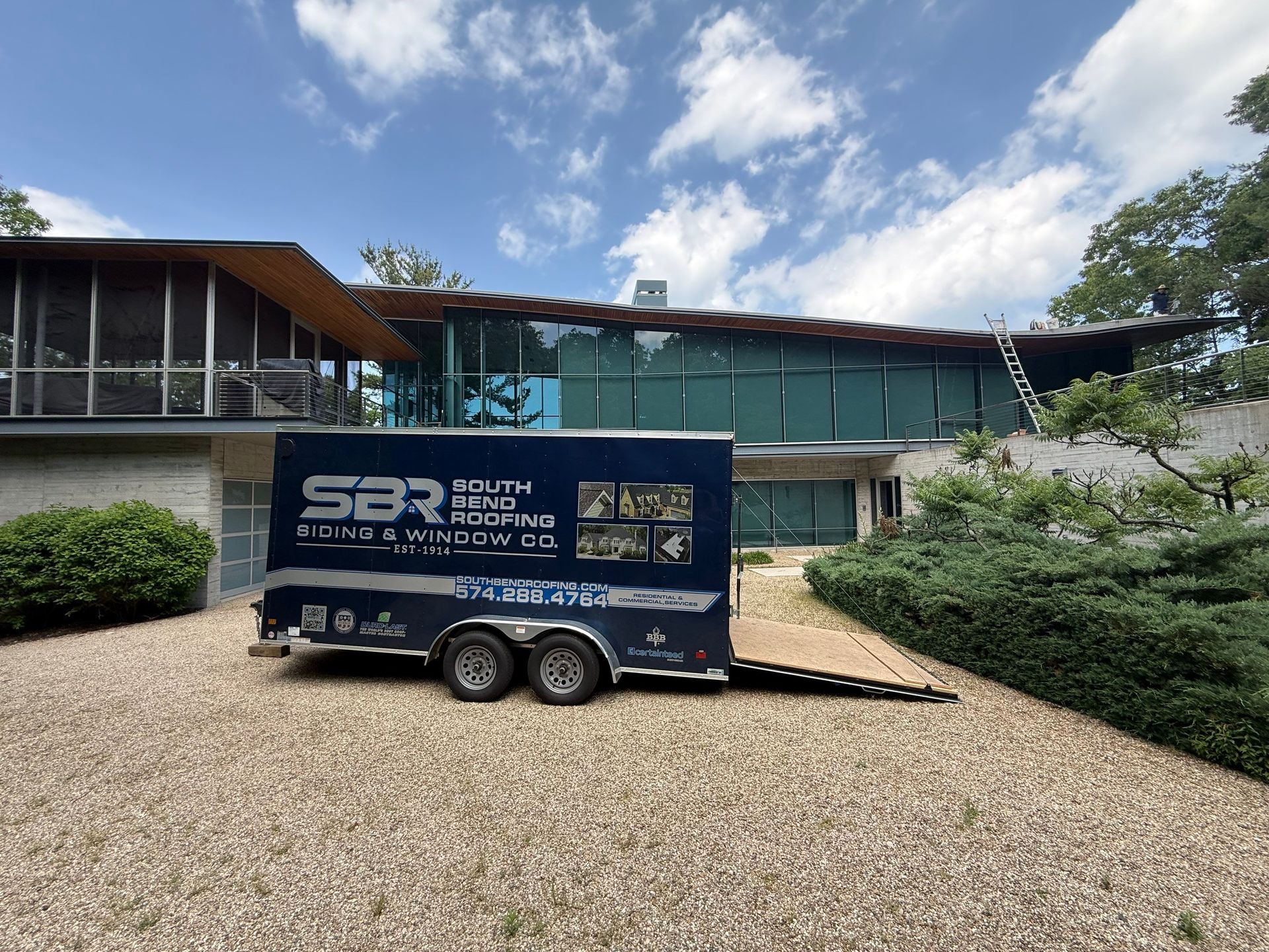 Blue trailer parked on gravel in front of a modern glass building under a partly cloudy sky