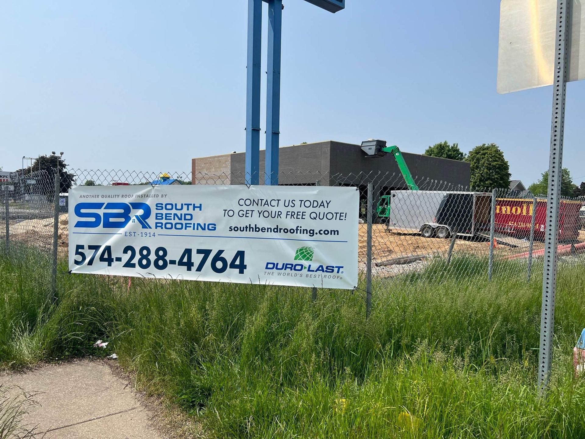 Sign for a construction company beside a grassy roadside lot under a blue sky