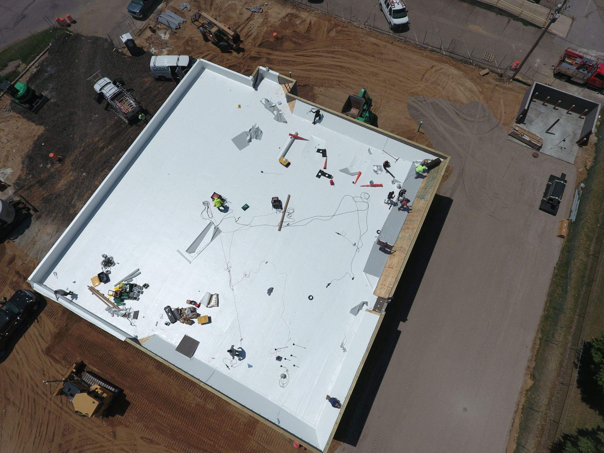 Aerial view of workers installing a white roof on a building at a construction site.