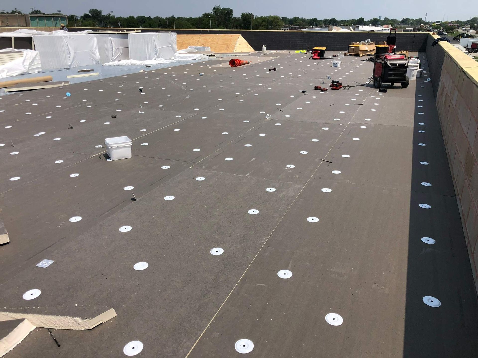 Flat rooftop under construction with workers, white fasteners, and equipment scattered across the surface.
