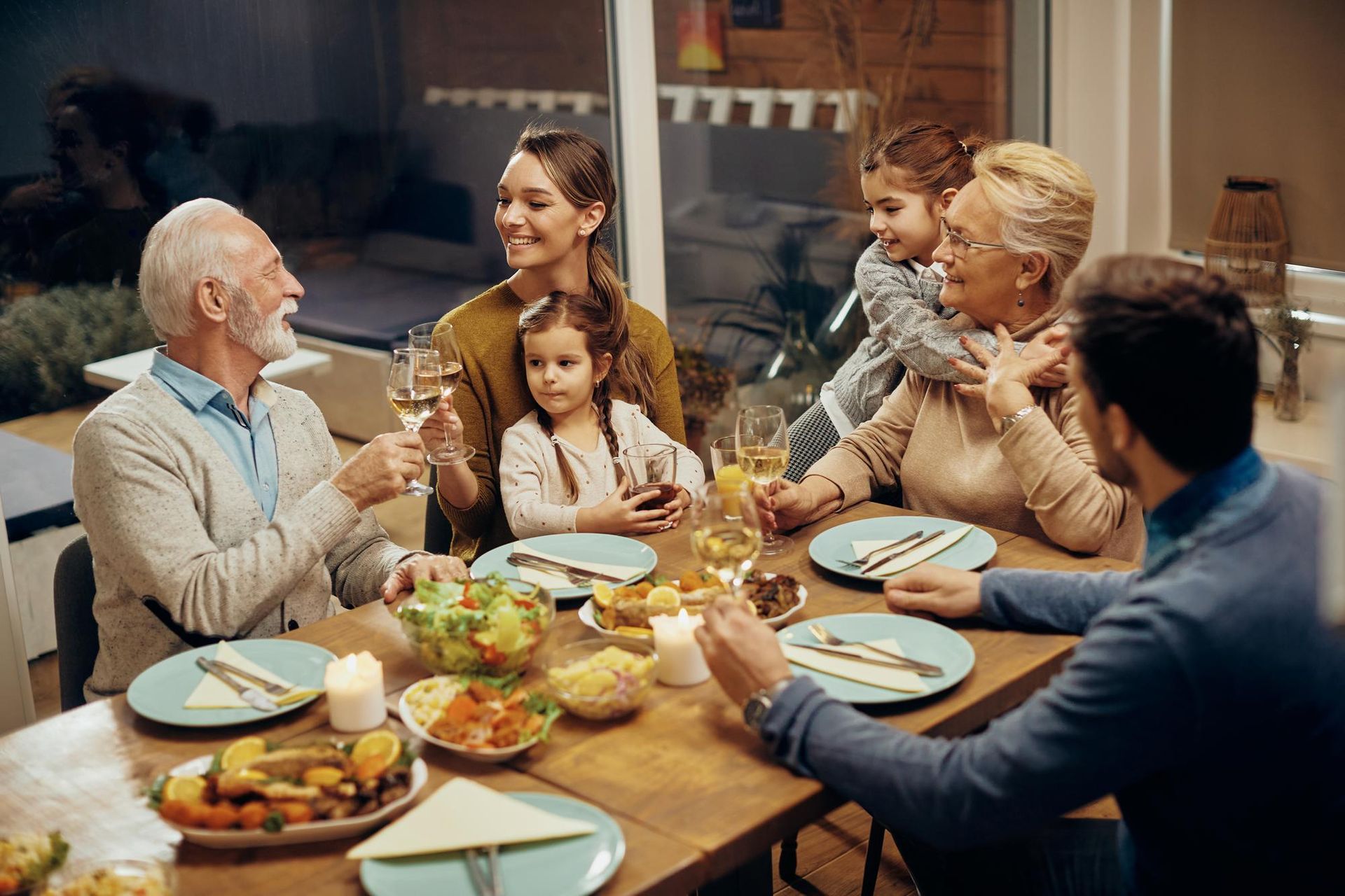 A multi-generational family enjoys a dinner party with toasts and wine, gathered around a table laden with food.