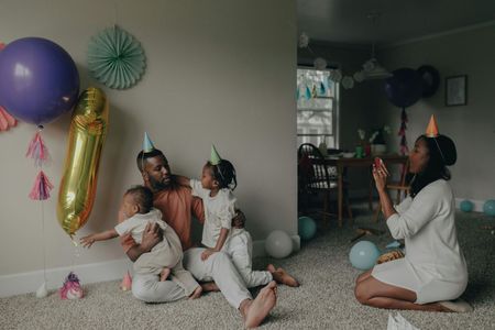 A smiling family of three relaxing together on a bed in a sunlit bedroom with a polka-dot wall.