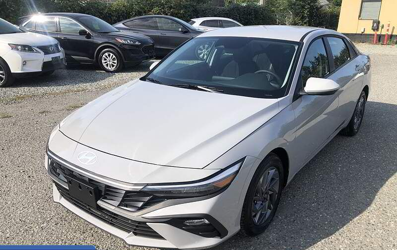 Light gray Hyundai sedan parked outdoors on a gravel lot. Other cars in the background.