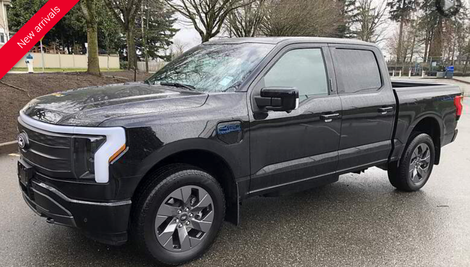 Black Ford F-150 Lightning pickup truck parked on a wet street.  White LED headlights, gray wheels, and a red 