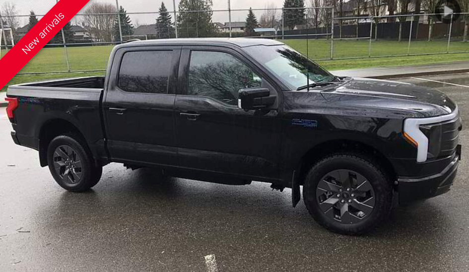 Black Ford F-150 Lightning pickup truck parked on a wet asphalt surface.