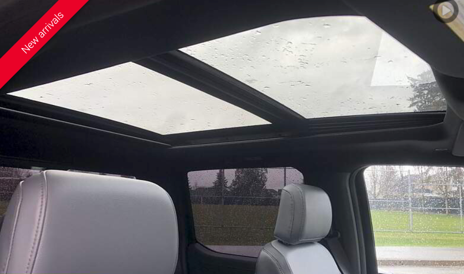 Interior of a truck with a panoramic sunroof, showing gray leather seats, and a view of the outside.