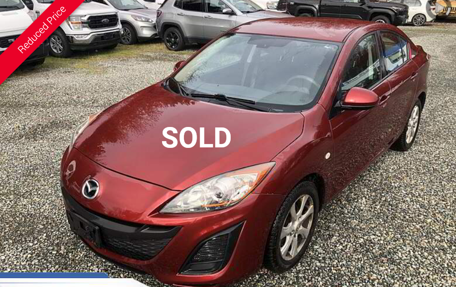 Red Mazda 3 sedan parked outside on gravel.